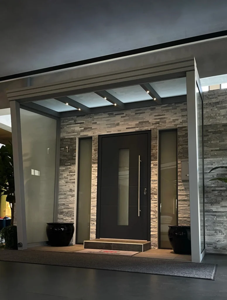 Moderne schwarze Villa-Haustür von Elsfen in Leverkusen mit Glasstreifen, Natursteinwand und beleuchtetem Eingangsbereich