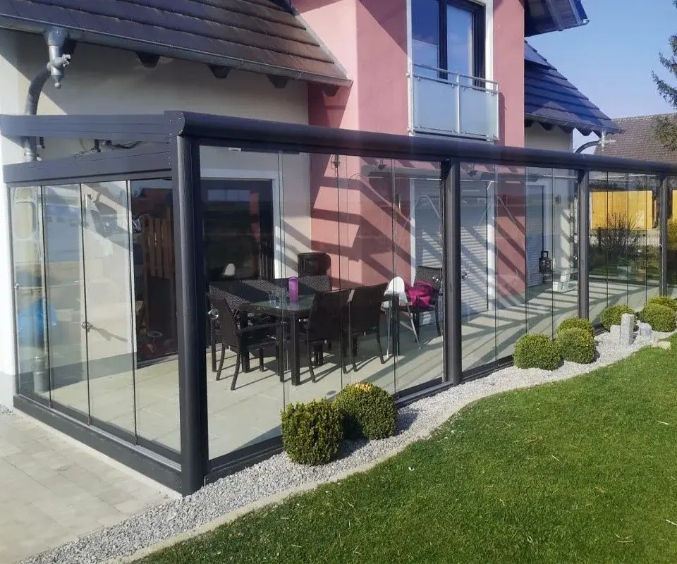 Eleganter Kaltwintergarten aus anthrazitfarbenem Aluminium mit Glasschiebetüren auf einer Terrasse in einem modernen Garten.