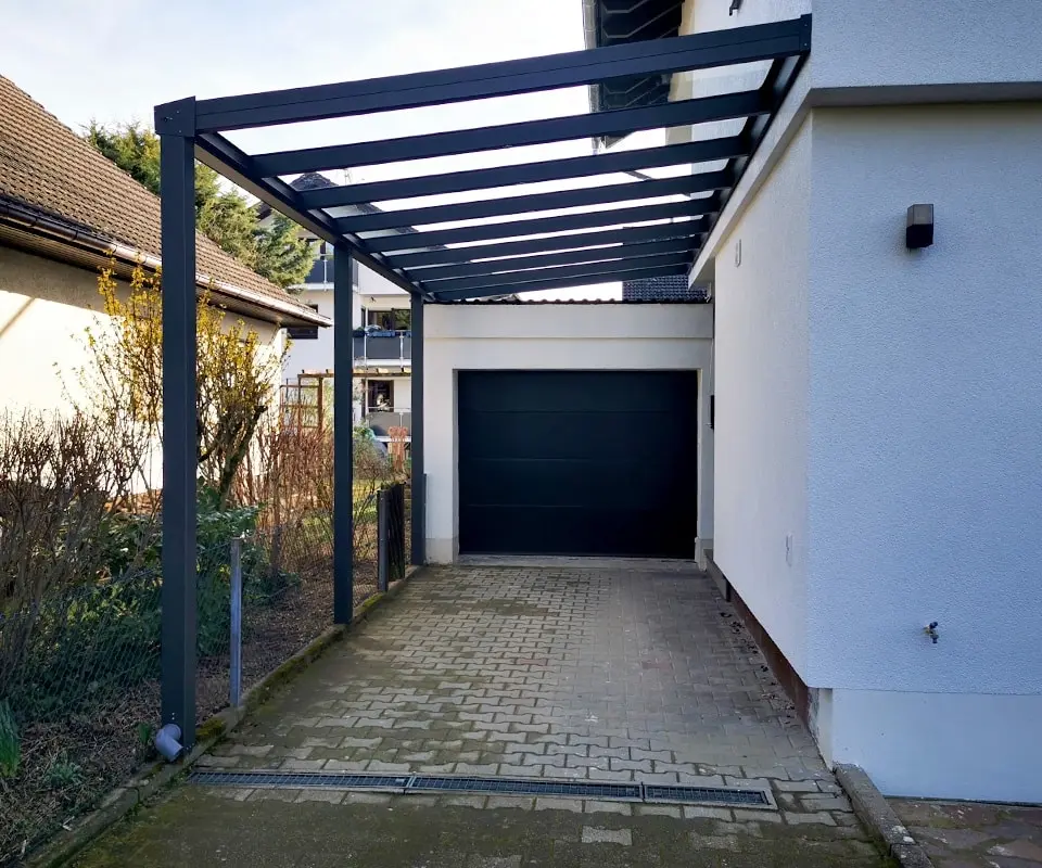 Anlehncarport aus Aluminium mit Stegplatten neben einem Garagentor in Köln