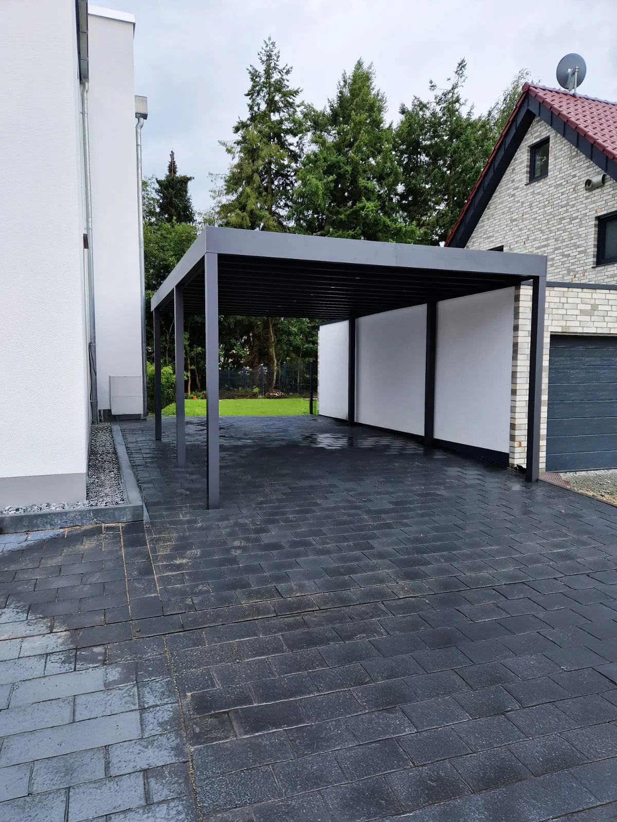 Doppelcarport mit weißen Sichtschutzpaneelen und dunklem Pflaster in Köln
