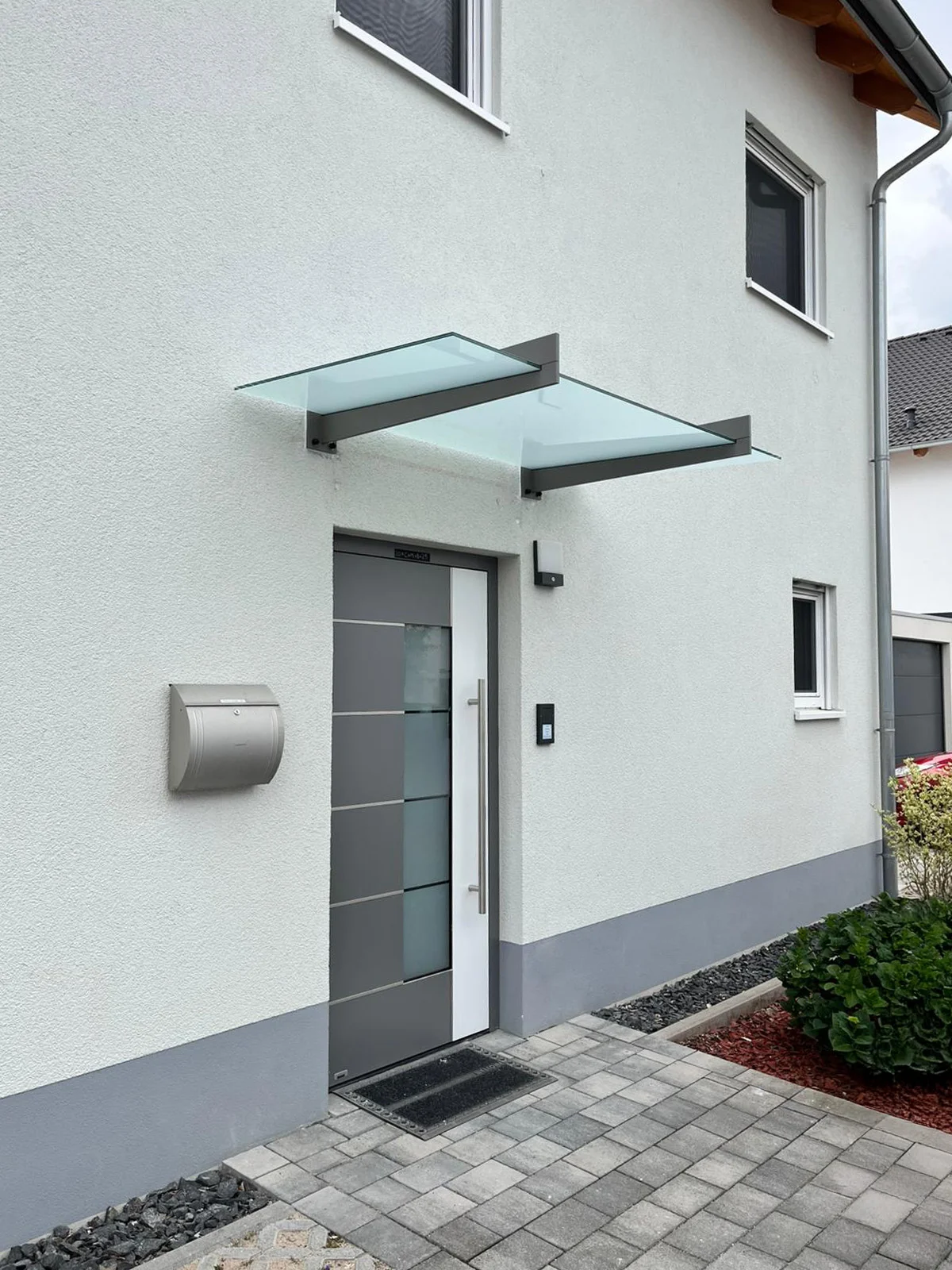 Glasvordach mit Seitenteil in Anthrazit an einem weißen Haus in Köln