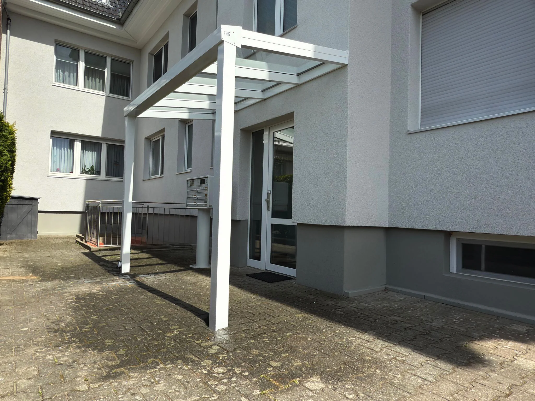 Weißes Aluminium-Vordach mit Glasdach an einem Mehrfamilienhaus in Köln